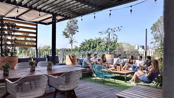 An outdoor patio area with seating arrangements, including a table and chairs, and a covered section with a pergola. - Nube Mia Hostel (Guadalajara)