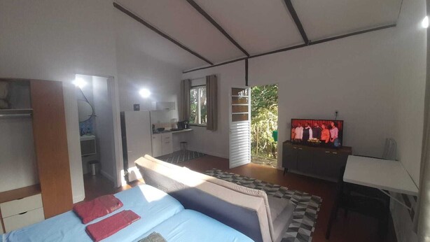 A bedroom with a bed, a desk, a television, and a kitchenette. - Cozy chalet surrounded by nature in a gated community (101) (Parque Rizzo Cotia)