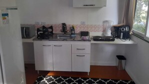 A compact kitchen with a microwave, kettle, coffee maker, and toaster on the countertop. - Cozy chalet surrounded by nature in a gated community (101) (Parque Rizzo Cotia)