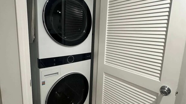 Une buanderie équipée d’un lave-linge et d’un sèche-linge superposés, d’une porte à panneaux ajourés et d’un sol carrelé.