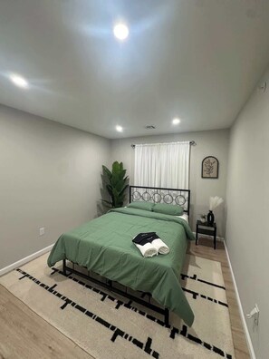 A neatly arranged bedroom with a bed, a bedside table, a potted plant, and a window with curtains. - Luxury 6BR Rooftop • Free Parking • Near NYC & EWR (Newark)
