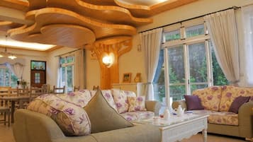 A cozy living room with a wooden ceiling, two sofas with floral upholstery, and a dining area in the background.