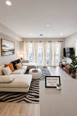 Een moderne woonkamer met een bank, een rond bijzettafeltje, een vloerkleed met zebraprint, een welkomstbord en een televisie.