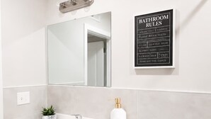Een badkamer met een witte wastafel, spiegel en toilet. Er hangt een bord met regels voor de badkamer aan de muur.