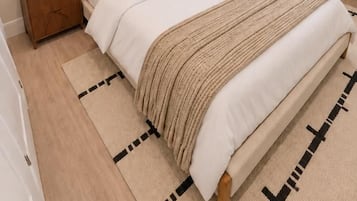 Une chambre à coucher bien rangée, avec un lit, des tables de chevet, une lampe, une plante et un tableau accroché au mur.