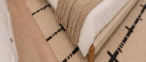 Un dormitorio ordenado con cama, mesitas de noche, una lámpara, una planta y un cuadro en la pared.