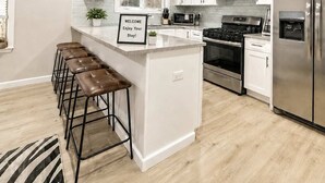 Een moderne keuken met witte kasten, een roestvrijstalen koelkast, een gasfornuis en een bar met krukjes.