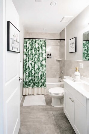 Une salle de bain moderne avec un rideau de douche, des toilettes, un lavabo et un tableau encadré au mur.