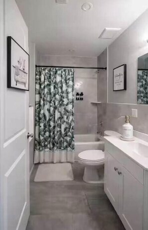 Une salle de bain équipée d’un rideau de douche, de toilettes, d’un lavabo et d’un meuble de rangement.