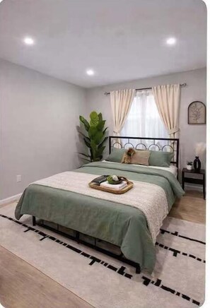 A bedroom with a bed, curtains, a plant, and a tray with items on the bed. - Cozy Rooftop Home, Near Downtown Newark, EWR & NYC (Newark)