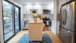 A modern kitchen with white cabinets, stainless steel appliances, and a central island with a vase of flowers. - Prime Location on Main Street (Stroudsburg)