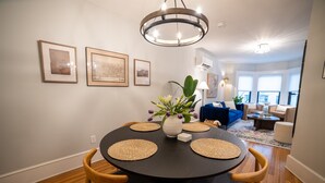 Ein Essbereich mit einem runden Tisch, Stühlen und einer Blumenvase. An der Wand befinden sich gerahmte Bilder und eine Chandelier hängt über dem Tisch.