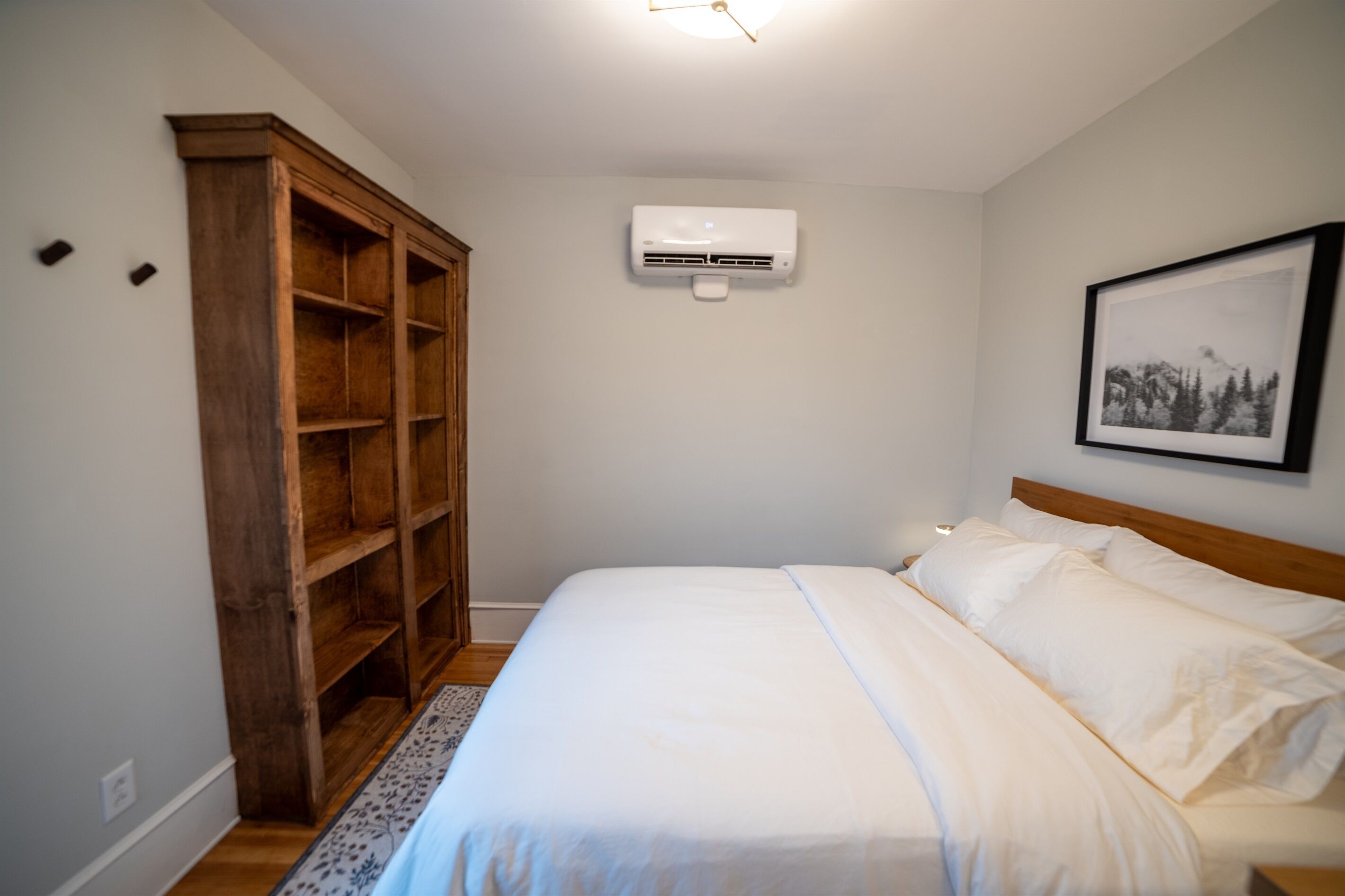 Une chambre à coucher comprenant un lit, une armoire en bois, un appareil de climatisation et un tableau encadré accroché au mur.