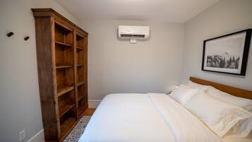 Une chambre à coucher comprenant un lit, une armoire en bois, un appareil de climatisation et un tableau encadré accroché au mur.