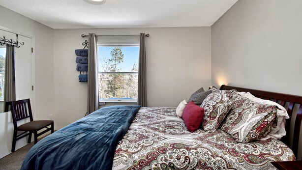 Een slaapkamer met een bed, een stoel, een raam met gordijnen en een wandlamp.