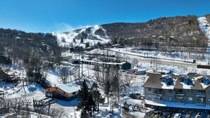 Ein großes Hotel mit mehreren Stockwerken, dahinter Skilifte und ein klarer, blauer Himmel.