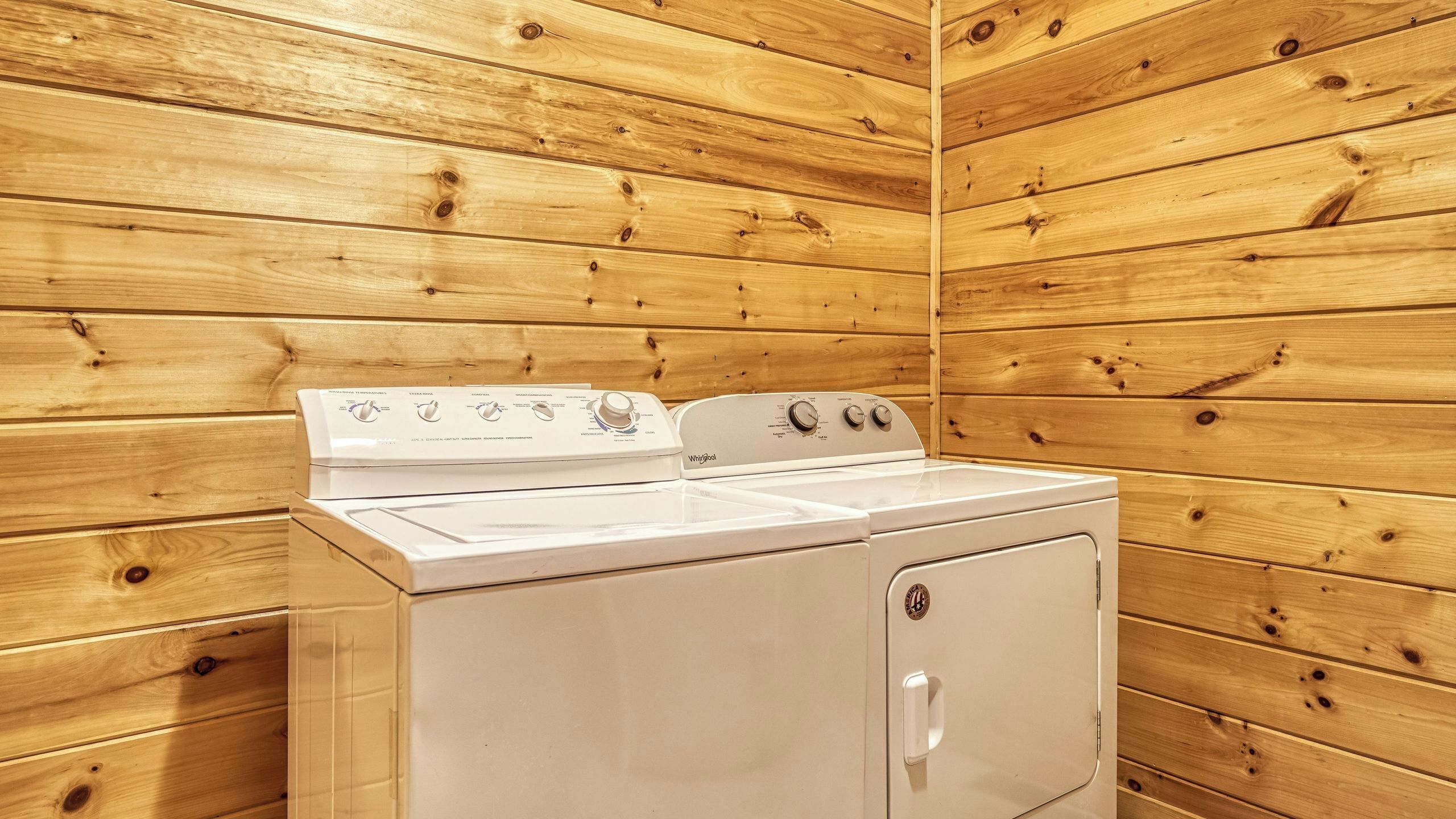 A kitchen with a stove and a washing machine, wooden walls, and a white countertop.