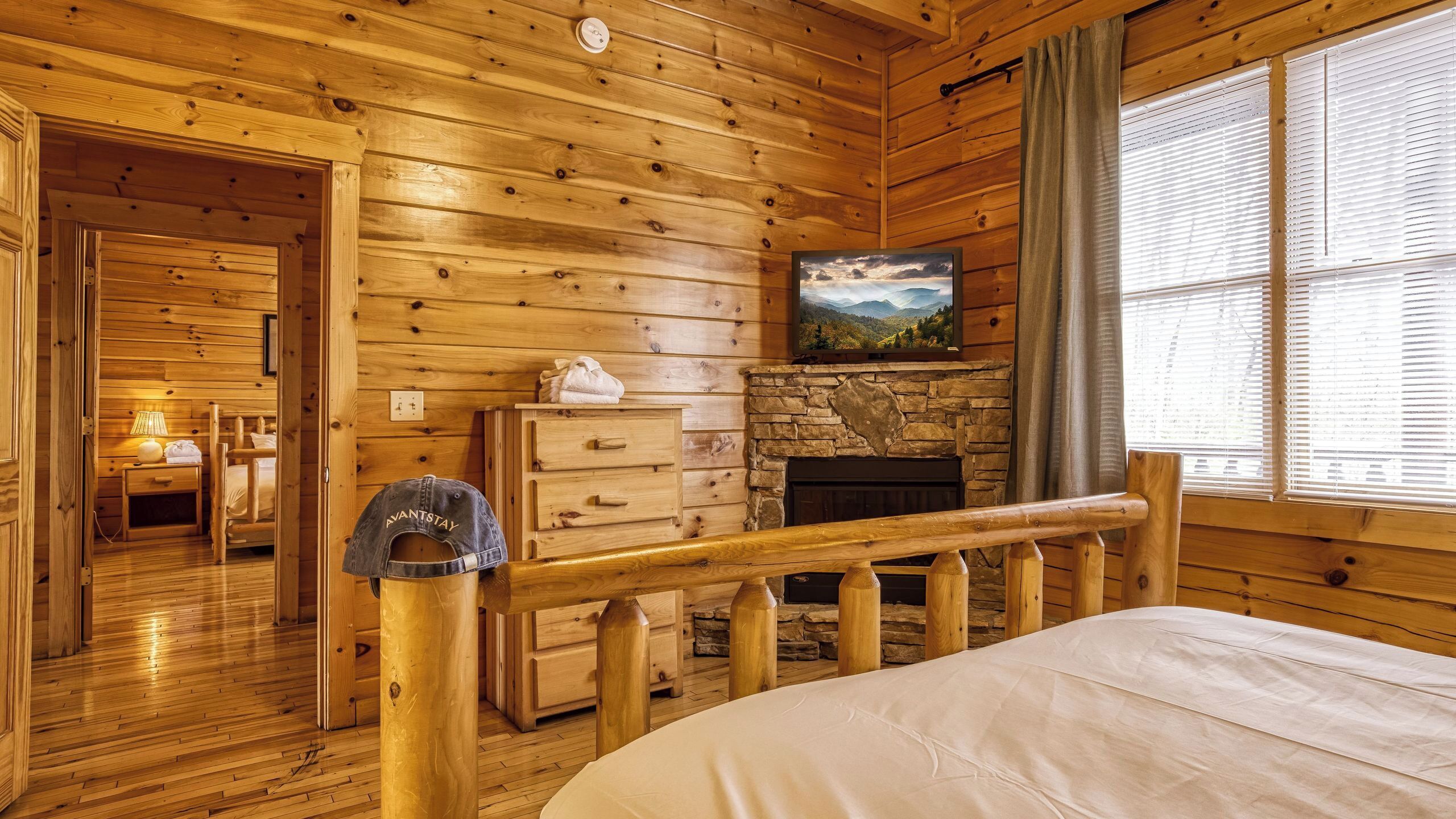 A wooden cabin room with a bed, a dresser, a fireplace, and a painting on the wall.