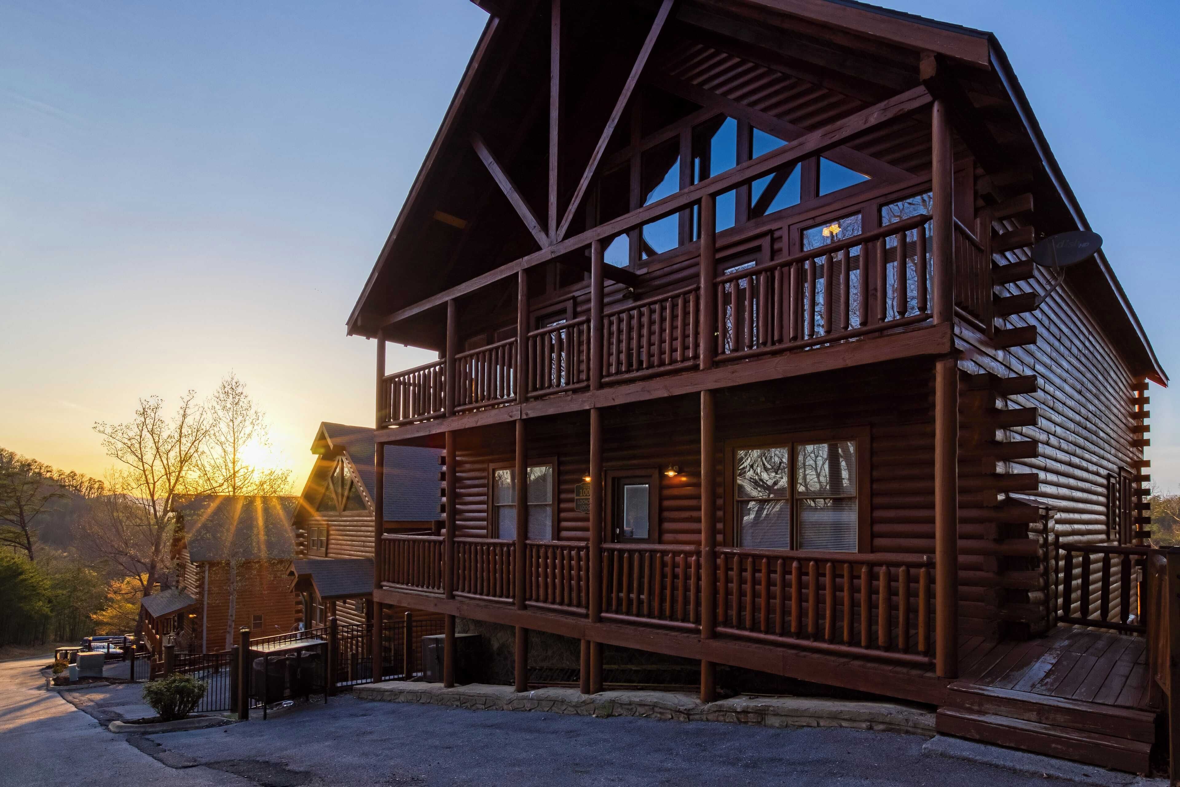 A two-story log cabin with a balcony, large windows, and a stone foundation.