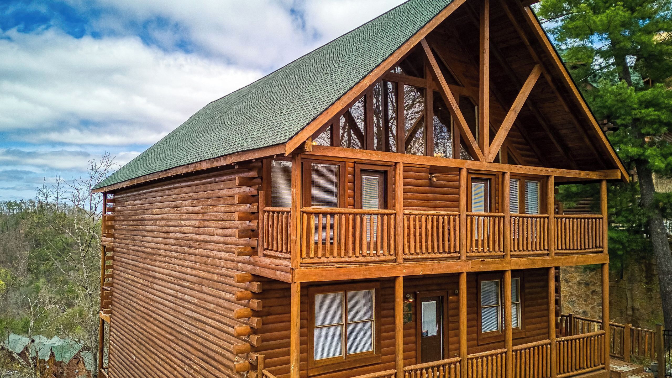 A log cabin with a balcony, multiple windows, and a steeply pitched roof.