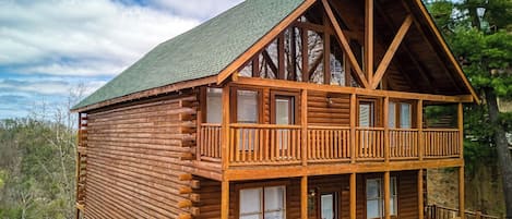 A log cabin with a balcony, multiple windows, and a steeply pitched roof.