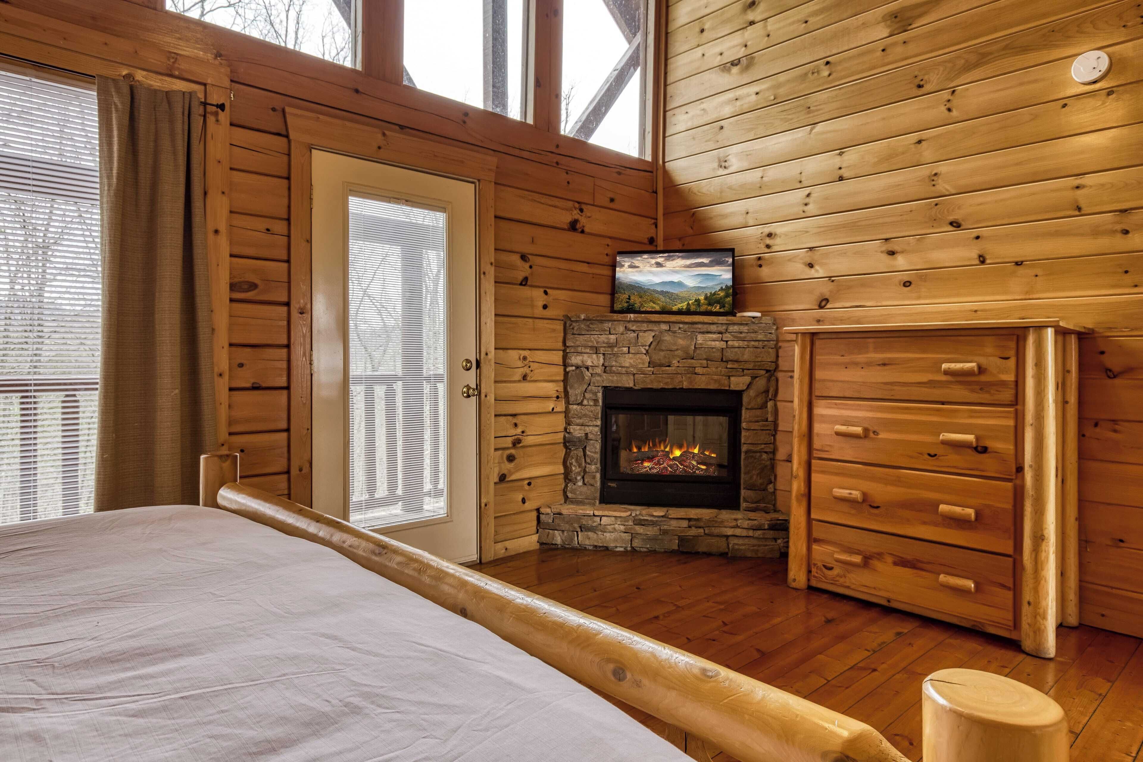 Una habitación tipo cabaña de troncos con chimenea de piedra, paredes de madera, una cama y una ventana con persianas.