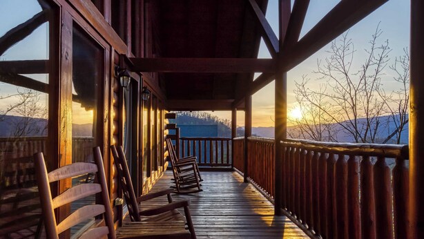 A wooden deck with chairs and a railing, overlooking a mountainous landscape during sunset. - Lookout Lodge by Avantstay Sleeps 18 Hot Tub Game Room Movie Theater View (Sevierville)