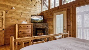 A log cabin room with a fireplace, wooden dresser, and a television mounted above it. - Lookout Lodge by Avantstay Sleeps 18 Hot Tub Game Room Movie Theater View (Sevierville)
