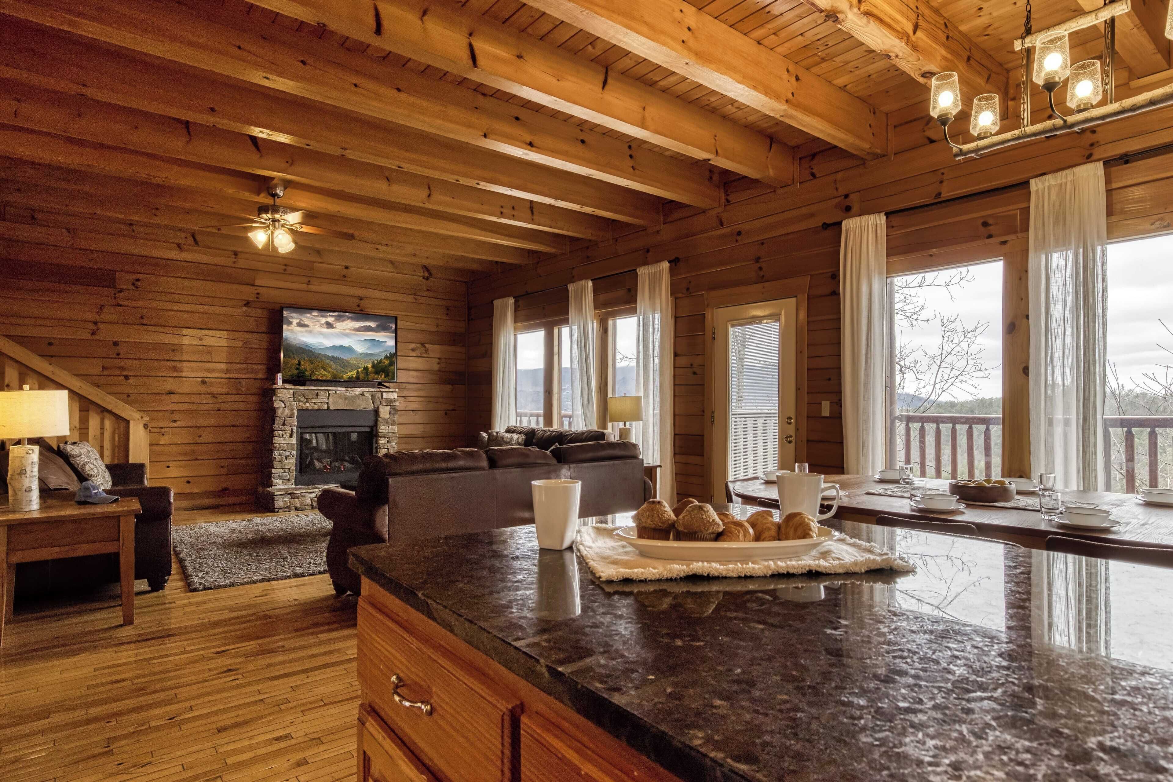 A wooden cabin interior with a stone fireplace, a dining area with a large island, and a cozy living room with a sofa and a television.
