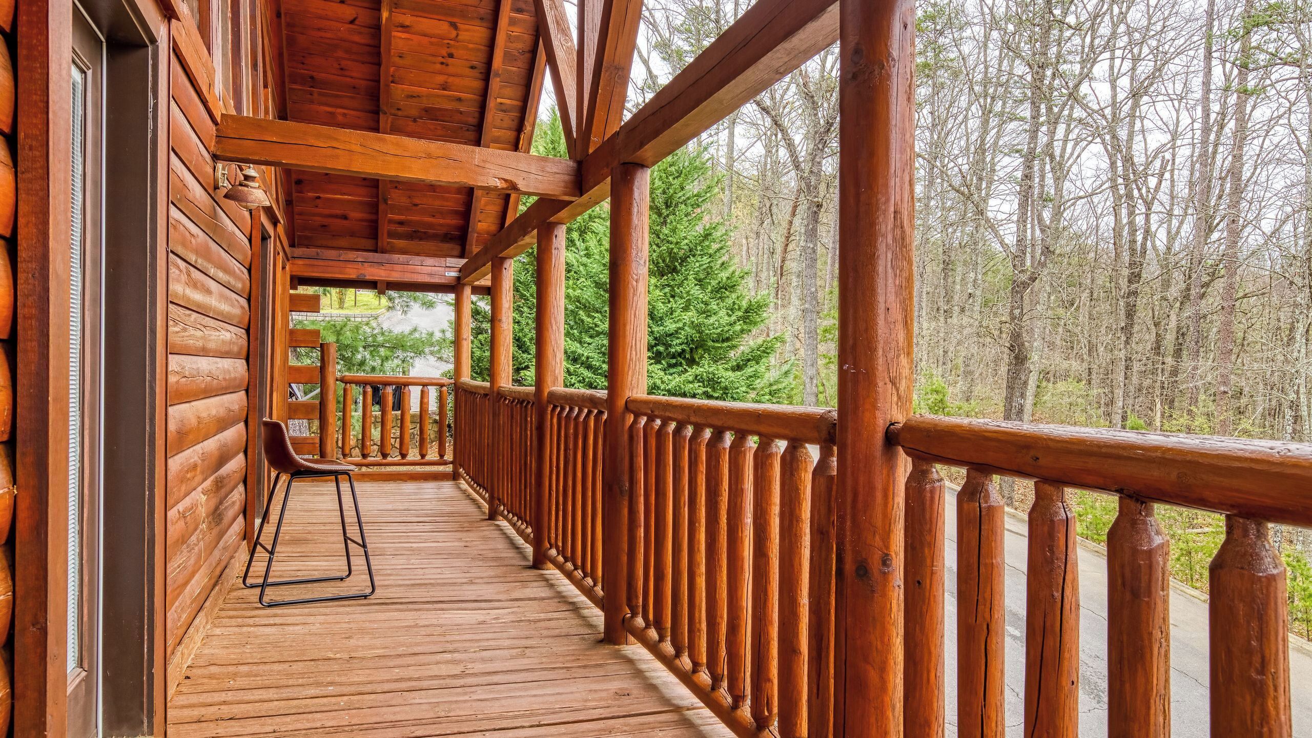A wooden cabin with a porch, a chair, and a view of a forest.