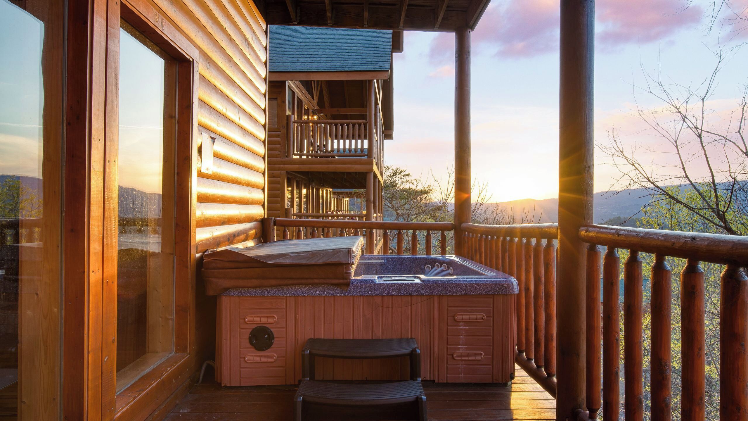 A wooden deck with a hot tub and seating area, overlooking a mountainous landscape.