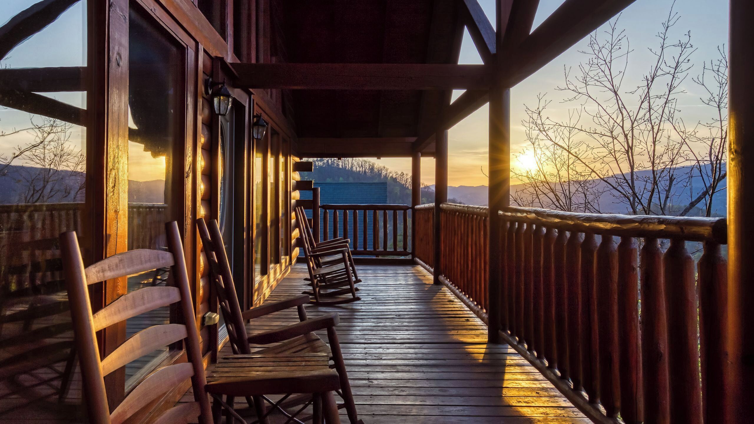 A wooden deck with chairs, a railing, and a view of mountains.