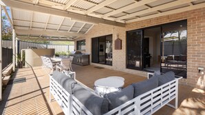 An outdoor patio area with a brick wall, a covered seating area with white furniture, and a grill. - Water Lane - Swimming Pool - 4 Mins Walk to Bay (Callala Bay)