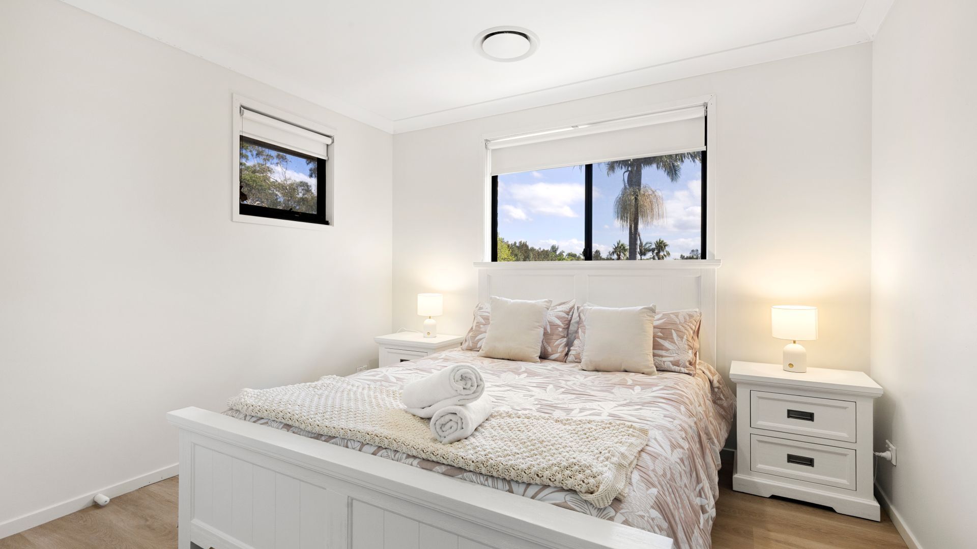 A bedroom with a bed, two bedside tables, a window with a view, and a ceiling light.