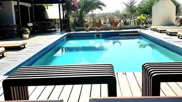 A rectangular swimming pool with a wooden deck and lounge chairs. - Niokobokk  (Ndiebene Gandiol)