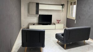 Ein modernes Wohnzimmer mit einem Flachbildfernseher, zwei schwarzen Sesseln und einer weißen Unterhaltungsanlage.