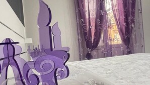 Ein Schlafzimmer mit einem Bett, violetten Vorhängen und einem dekorativen violetten Kopfteil.