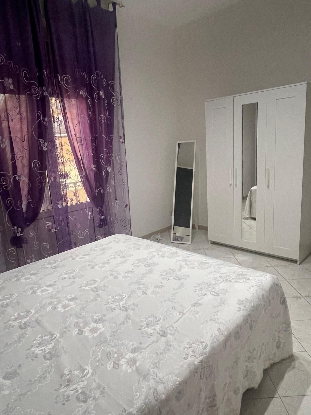 A bedroom with a bed, a wardrobe, and a full-length mirror.