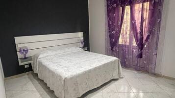 Una camera da letto con un letto, un comodino, una finestra con tende viola e un lucernario.