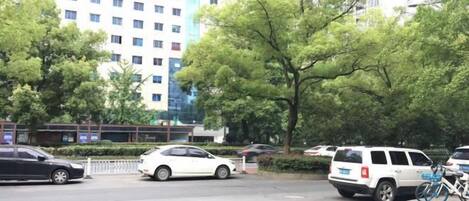Un parking avec plusieurs voitures, un bâtiment en arrière-plan et des arbres.