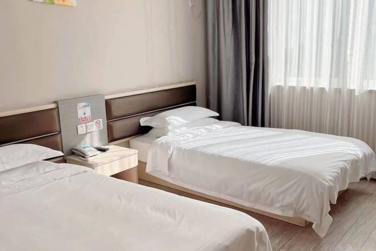 Habitación de hotel con dos camas, una mesita de noche, un espejo y una ventana con cortinas.