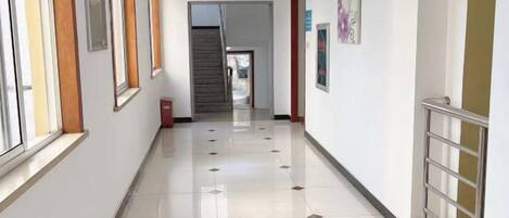 Un pasillo con una escalera, un bote de basura y un letrero que indica una salida.