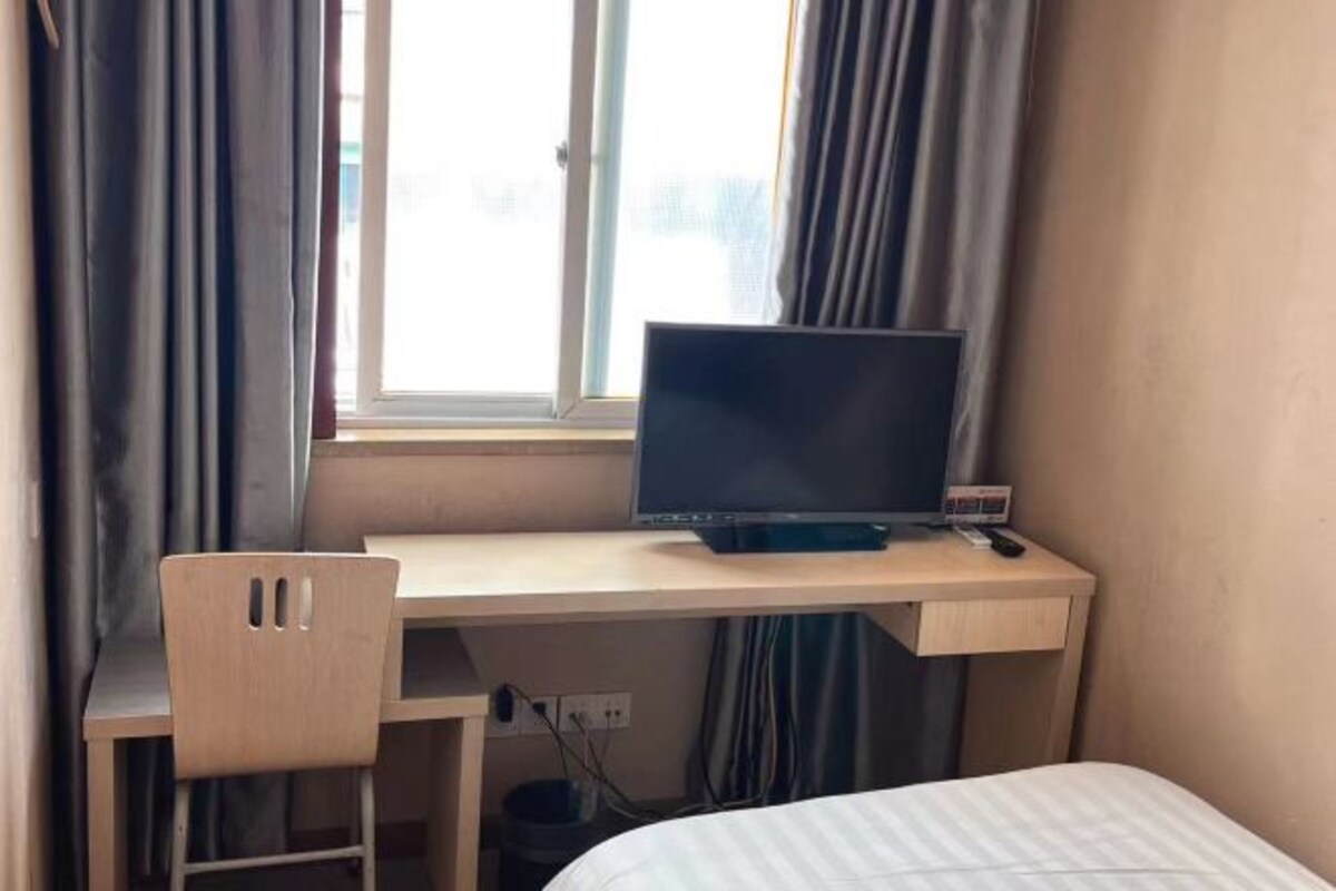 A room with a bed, a desk with a computer, and a chair.