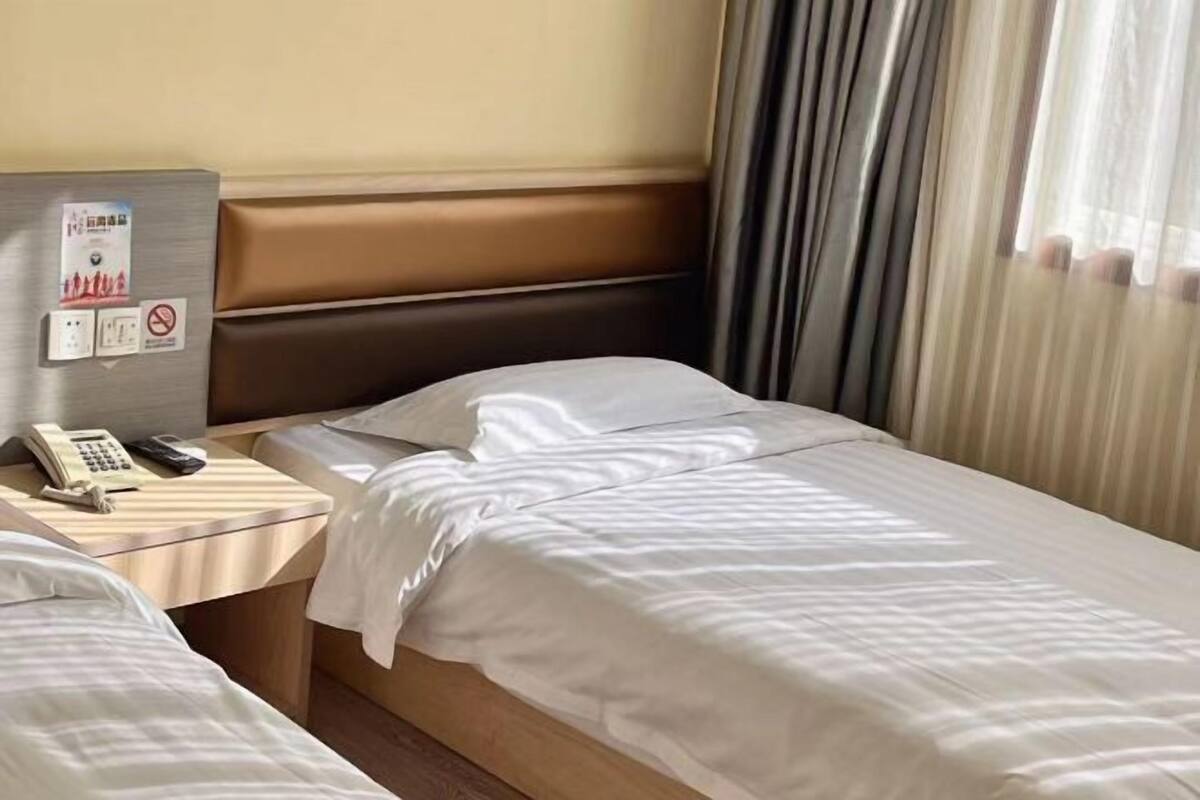 Una habitación de hotel con cama, mesita de noche con teléfono y panel en la pared con un cartel.