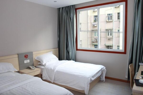 A hotel room with two beds, a window with a view of buildings, a nightstand with a phone, and a chair.
