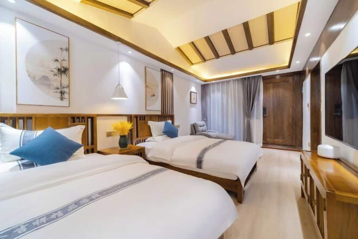 A hotel room with two beds, wooden headboards, a large window with curtains, and a wooden dresser.
