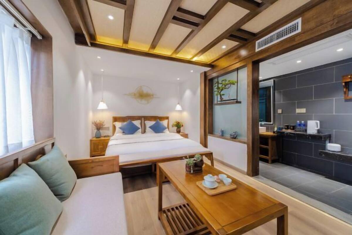 A modern hotel room with a bed, bedside table, and a small kitchenette.
