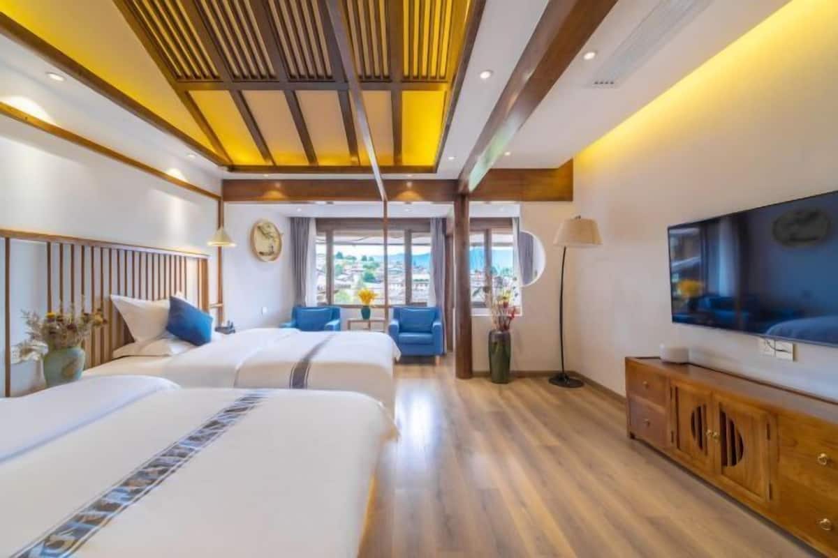 A hotel room with two beds, a TV, a wooden cabinet, and a view of the outdoors.