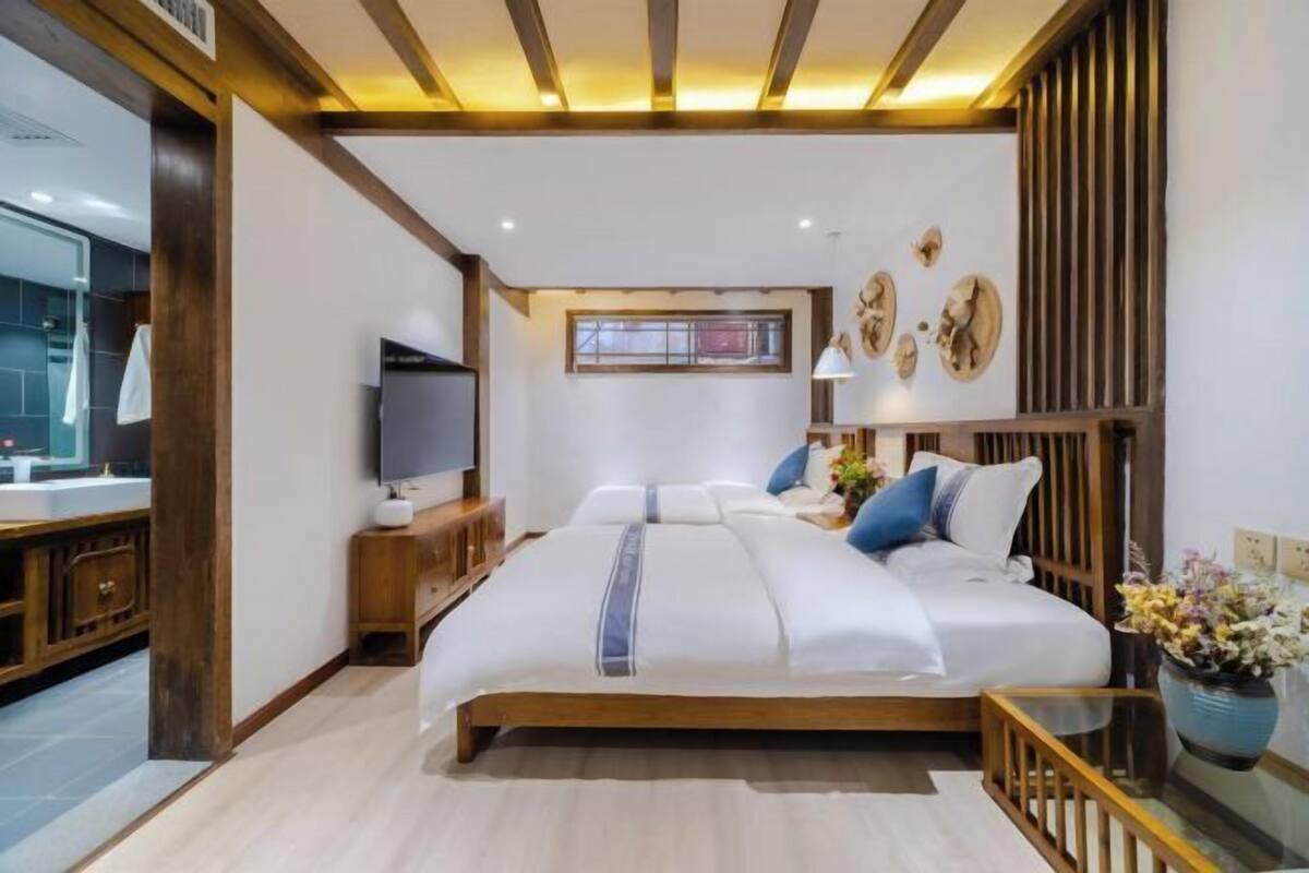 A bedroom with a large bed, a TV, a window, and a wooden headboard.