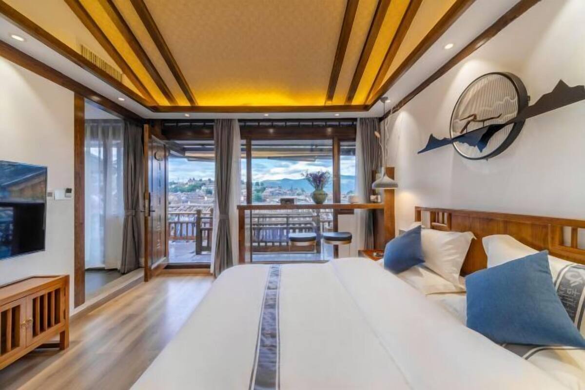 A hotel room with a large bed, a TV, a balcony with a view, and a clock on the wall.